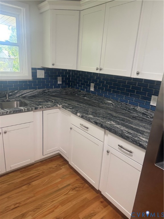 White shaker-style cabinetry, dark patterned countertops, blue subway tile backsplash, and wood-finish flooring White shaker-style cabinetry, dark patterned countertops, blue subway tile backsplash, and wood-finish flooring