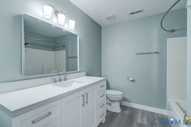 White vanity with integrated sink, contemporary polished chrome faucet, rectangular framed mirror, and wood-finish flooring