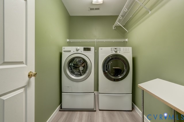Laundry area featuring wood-finish flooring, two large appliances, overhead wire shelving, and a built-in folding counter