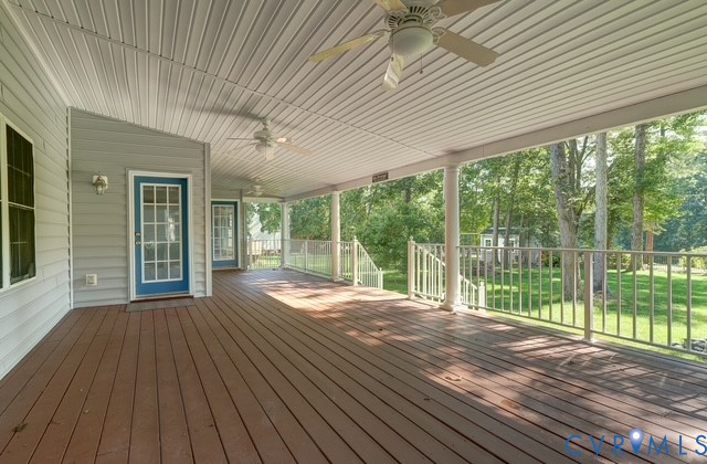 Expansive covered deck with wood-finish flooring, multiple ceiling fans, and a white railing system