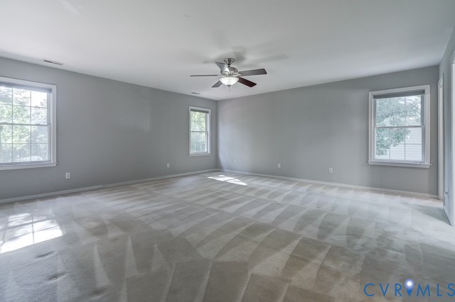 Expansive room featuring light gray wall paint, light-toned carpeting, multiple windows, and a ceiling fan with integrated lighting