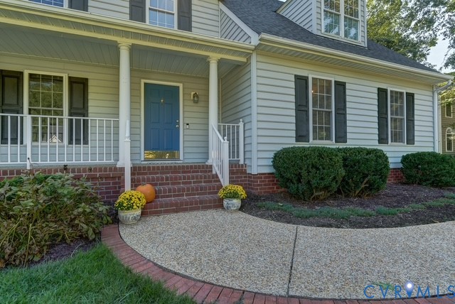 Light-colored siding exterior with dark shutters, brick foundation, and a covered porch