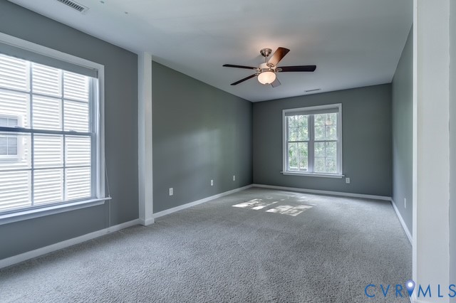 Spacious room featuring neutral wall tones, plush carpeting, multiple windows, a ceiling fan, and white trim accents
