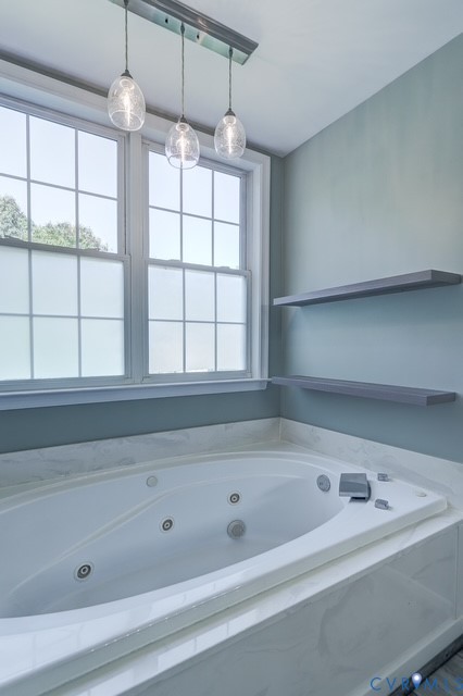 Soaking tub with integrated jets, white window frames, modern pendant light fixture, two floating shelves, and a white countertop surround