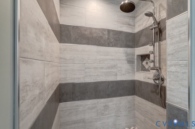Tiled shower stall featuring a rainfall showerhead, handheld shower, built-in niche with mosaic tile, and chrome fixtures