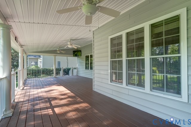 Expansive covered porch featuring wood-finish flooring, white architectural columns, multiple ceiling fans, horizontal siding, and multiple large windows
