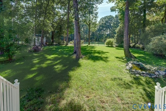 Expansive lawn with mature trees, a decorative rock-lined water feature, and a shed in the background