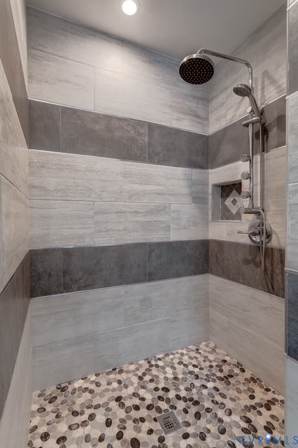 Shower enclosure with striped tile walls, pebble-finish flooring, recessed lighting, rainfall showerhead, and a built-in niche with decorative tile