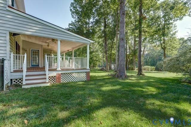 Expansive rear yard with mature trees and a covered deck featuring white railings, lattice skirting, and brick accents