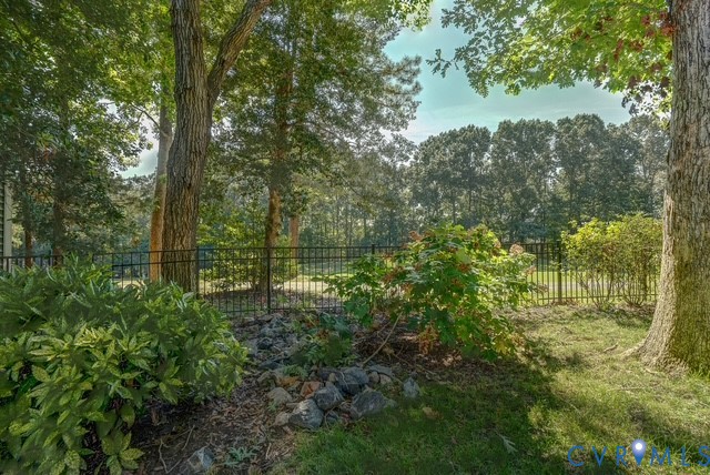 Expansive exterior featuring mature trees, a manicured lawn, and a black metal fence