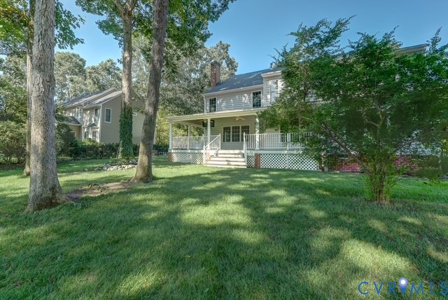 Expansive rear yard with mature trees and a covered porch featuring white railings
