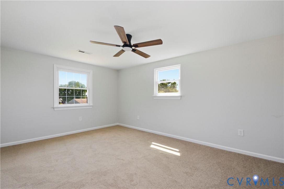 Neutral paint palette with carpeted flooring, featuring two windows and a ceiling fan