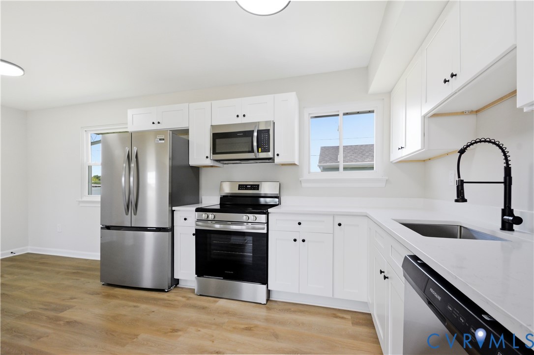 Kitchen featuring white cabinetry, stainless steel appliances, white countertops, a stainless steel sink with a black coiled faucet, and wood-finish flooring
