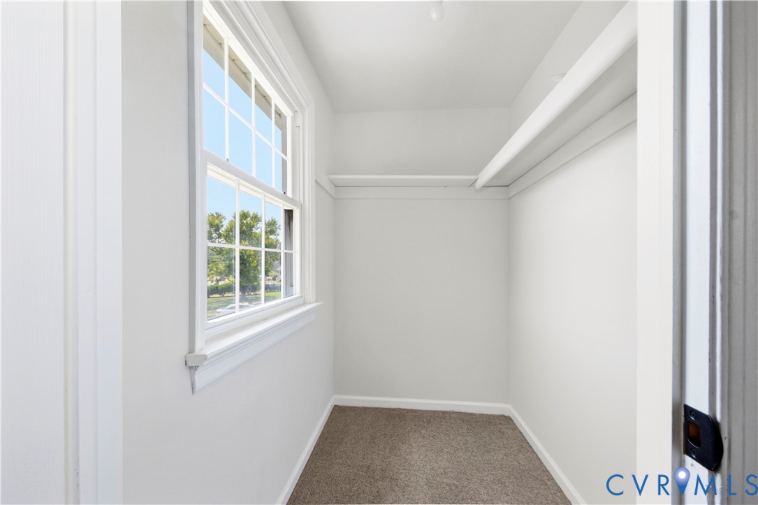 Windowed closet with carpet flooring and built-in shelving