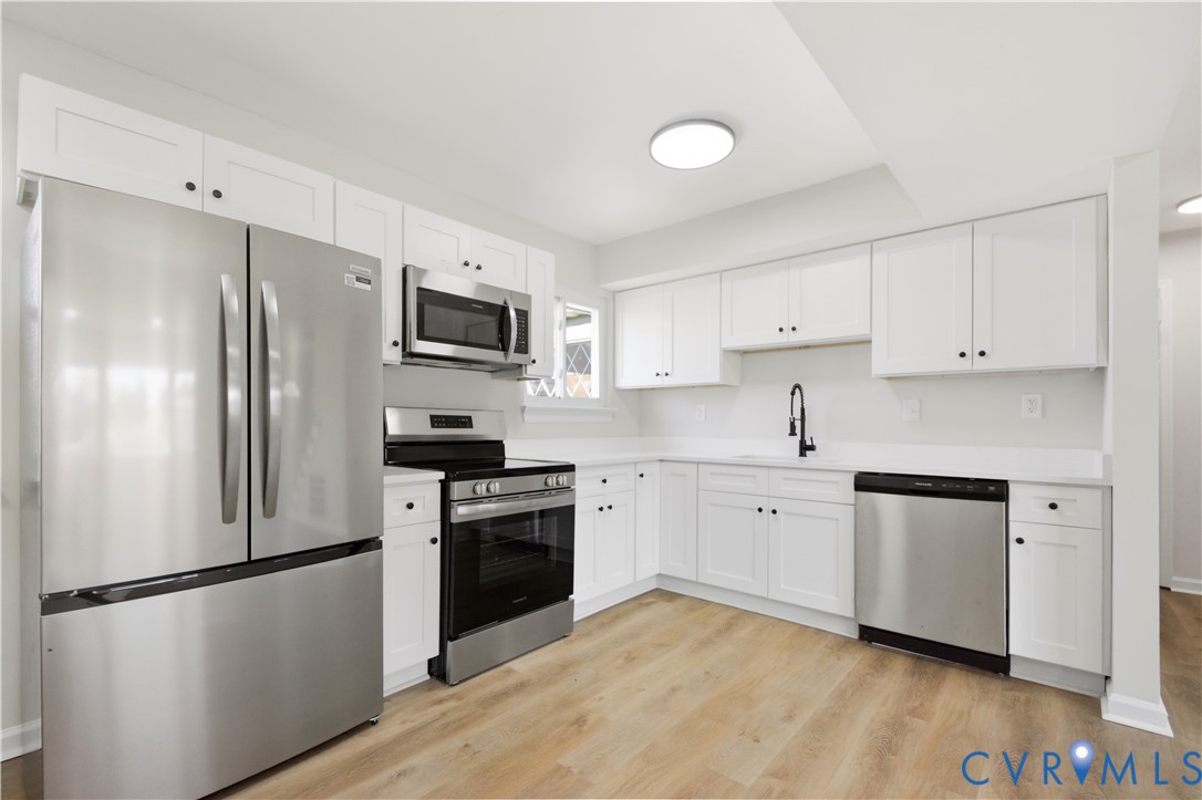 Kitchen featuring stainless steel appliances, white cabinetry, a matte black faucet, and wood-finish flooring