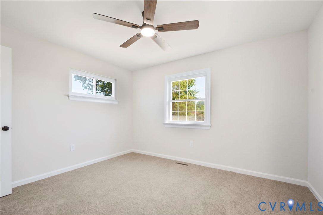 Neutral toned carpeting complemented by bright white walls, two windows with white trim, a modern ceiling fan with integrated lighting, and a white door with a black doorknob