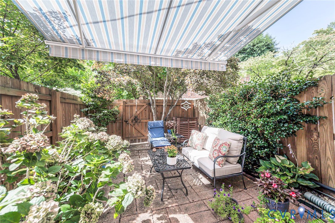 Paved patio featuring a striped retractable awning, privacy fencing, and established plantings