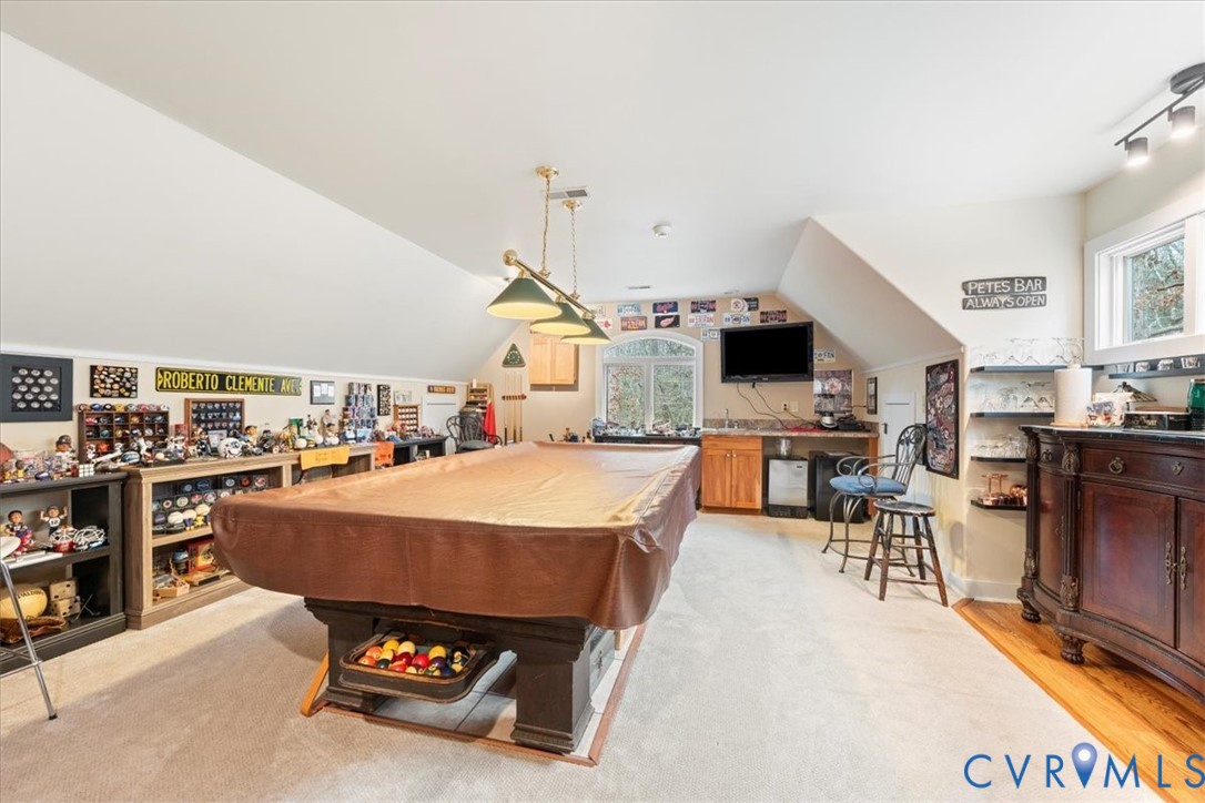 Sloped ceilings, wall-mounted track lighting, built-in wet bar, wood-finish flooring, and a window with arched transom