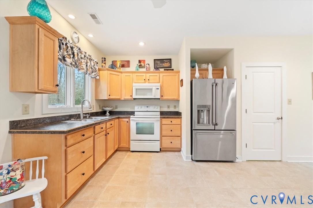 Kitchen featuring hardwood cabinetry, dark countertops, a double basin stainless steel sink, and stainless steel refrigerator