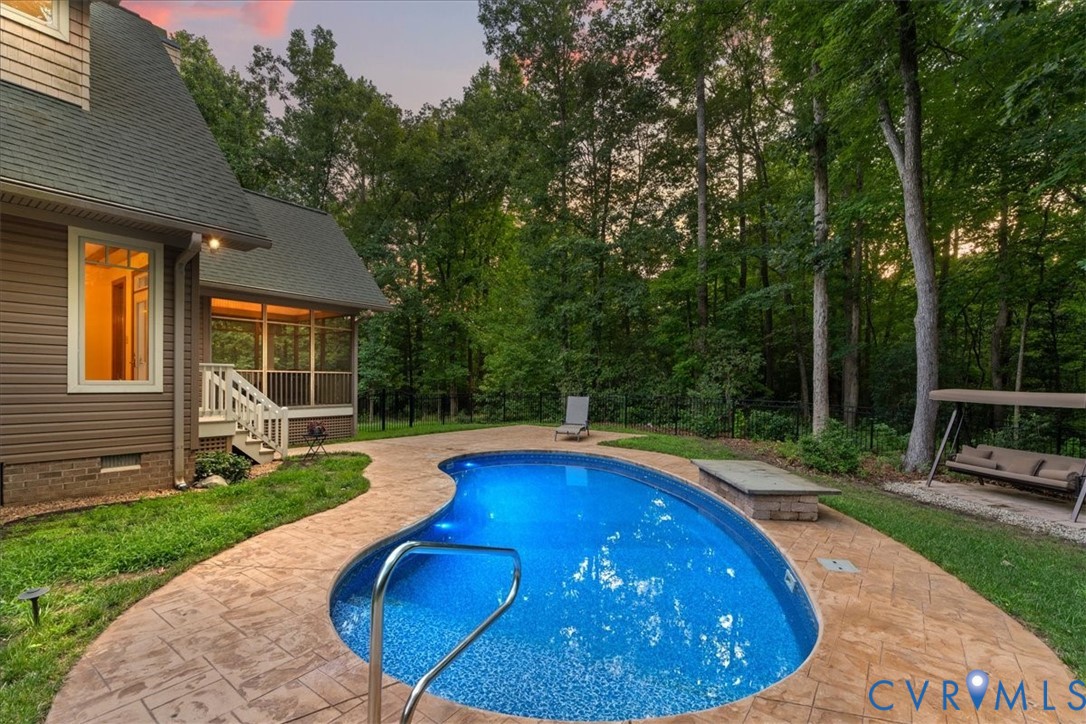 Freeform inground pool with an adjacent stamped concrete patio, screened porch, and mature trees surrounding the property