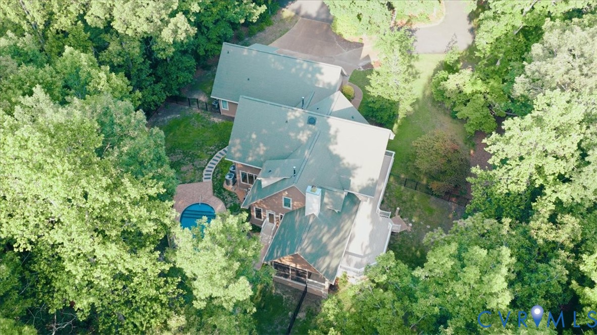 Expansive property featuring a multi-level structure, a circular pool with surrounding hardscaping, and a lush, tree-lined perimeter