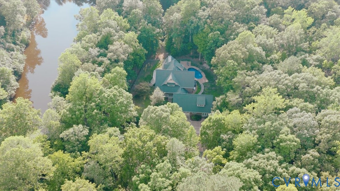 Spacious property surrounded by lush green trees, featuring a residence with a dark roof, an outdoor pool, and a private driveway