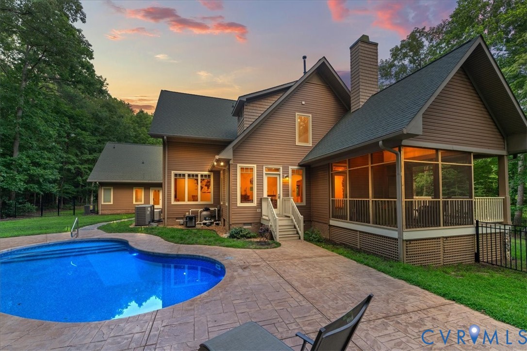 Rear exterior with a freeform swimming pool, stamped concrete patio, screened porch, and mature trees