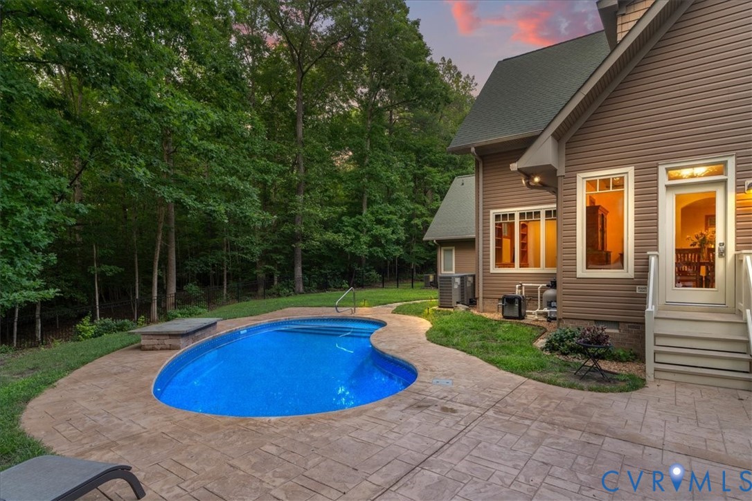 Exterior featuring a swimming pool, stamped concrete patio, and a stone-clad raised planter/ Heater pool