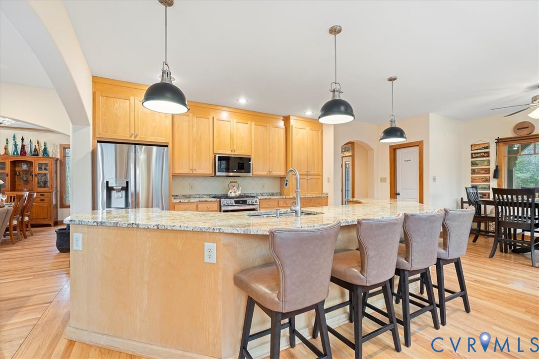 Open-concept kitchen featuring an island with seating, stainless steel appliances, light wood cabinetry, and wood-finish flooring