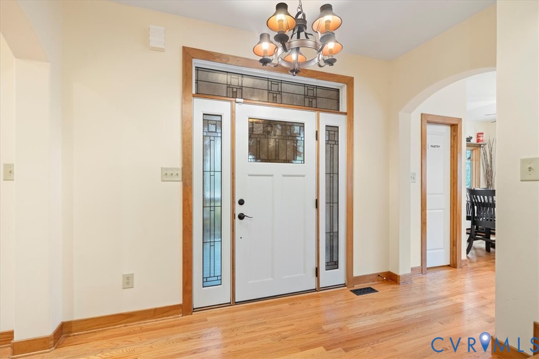Entryway featuring a decorative transom, sidelight windows, a chandelier, hardwood flooring, and an arched doorway