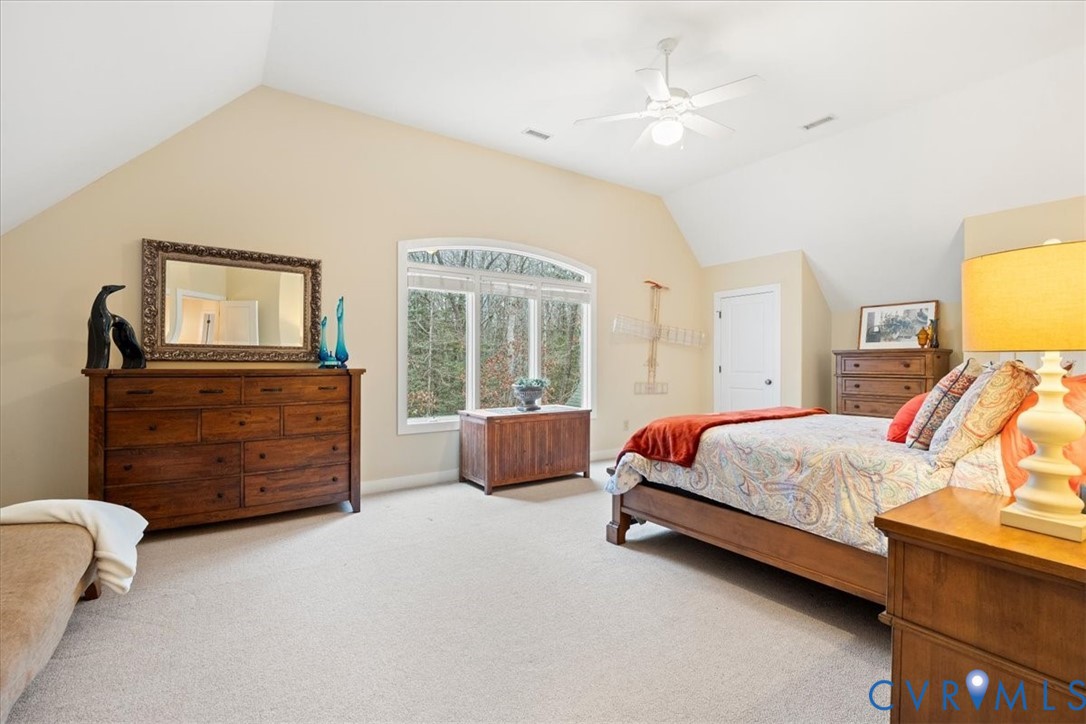 Vaulted ceiling with ceiling fan, arched window, and neutral carpeting
