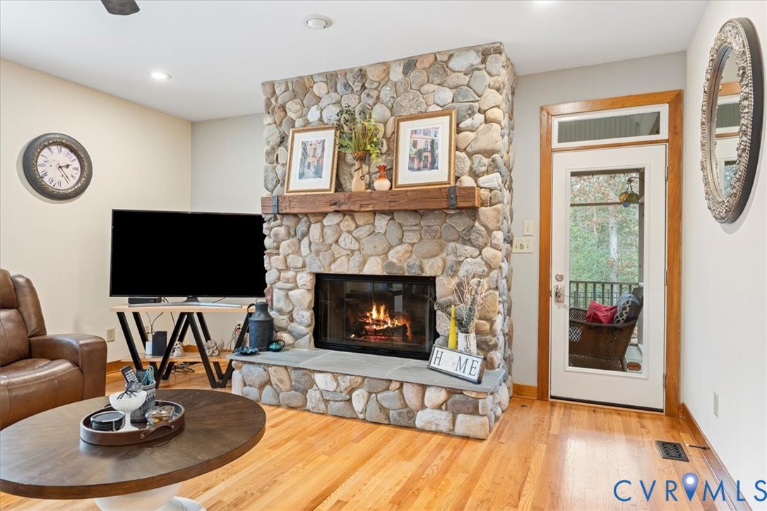 Stone-clad fireplace with a wood mantel, hardwood flooring, and recessed lighting