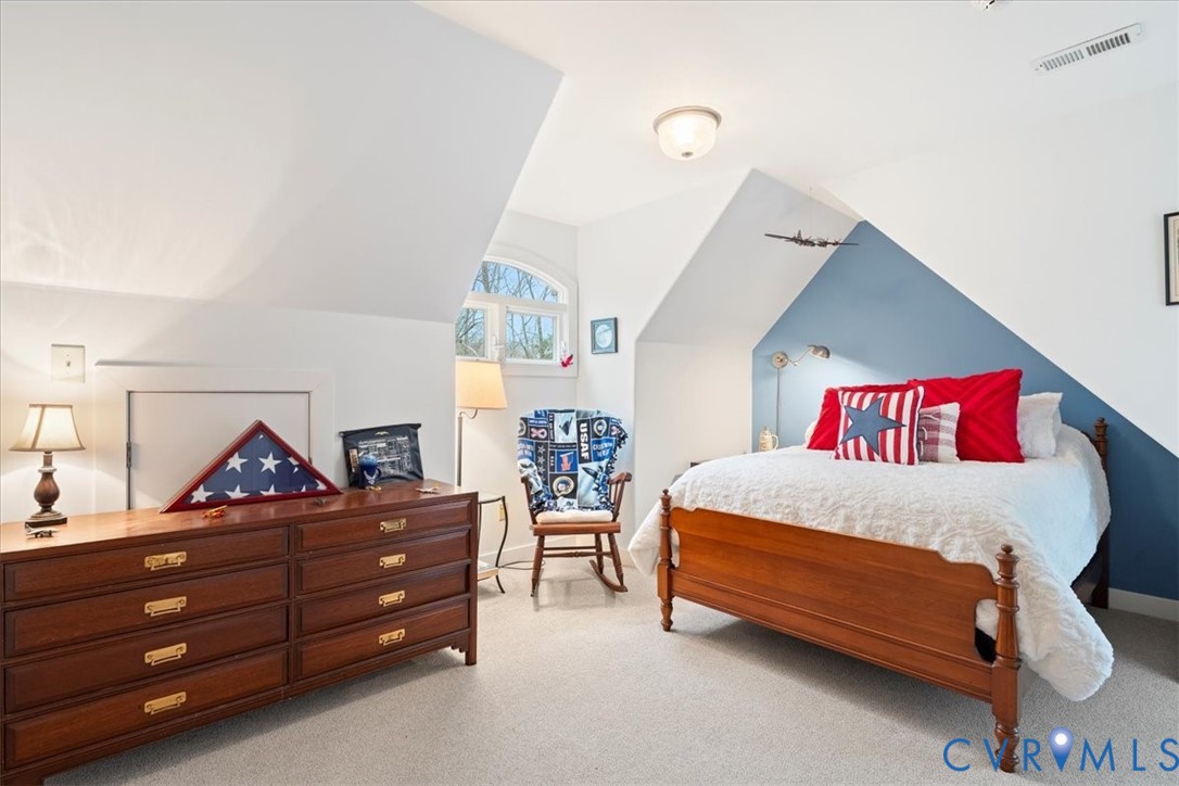 Sloped ceiling architecture, arched window, wall-mounted light fixtures, built-in storage access panel, and wood-finish flooring