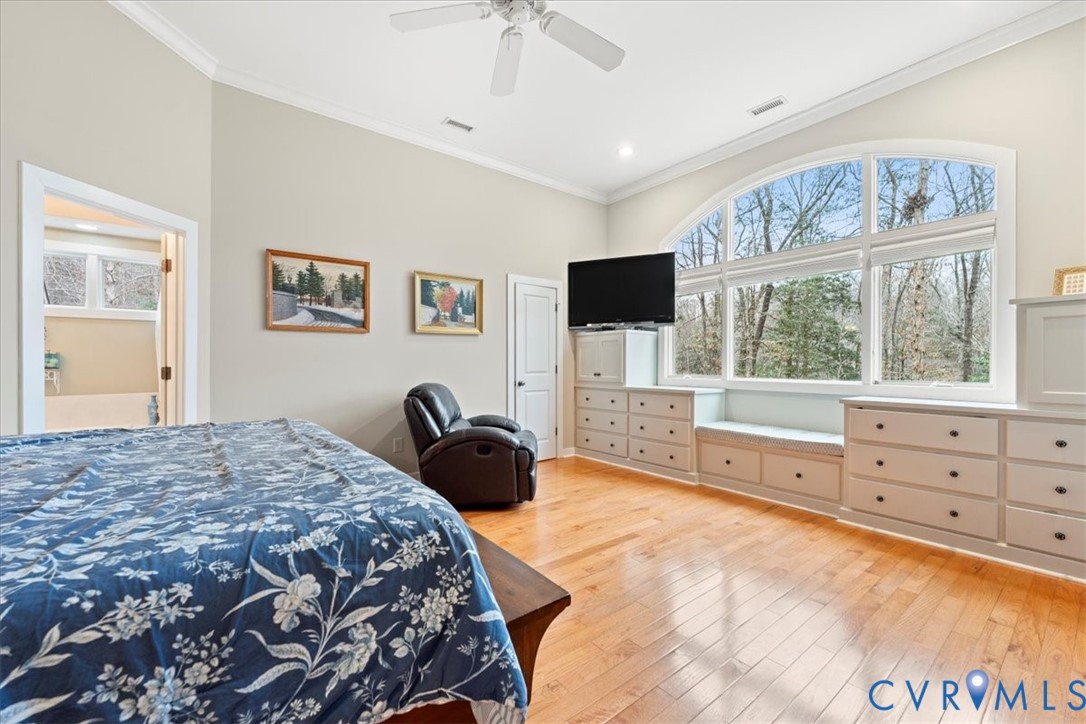 Hardwood flooring, arched window, built-in cabinetry, crown molding, and a ceiling fan