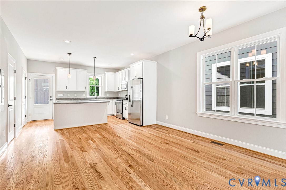 Open concept living area with wood-finish flooring, white cabinetry, stainless steel appliances, and a kitchen island Open concept living area with wood-finish flooring, white cabinetry, stainless steel appliances, and a kitchen island
