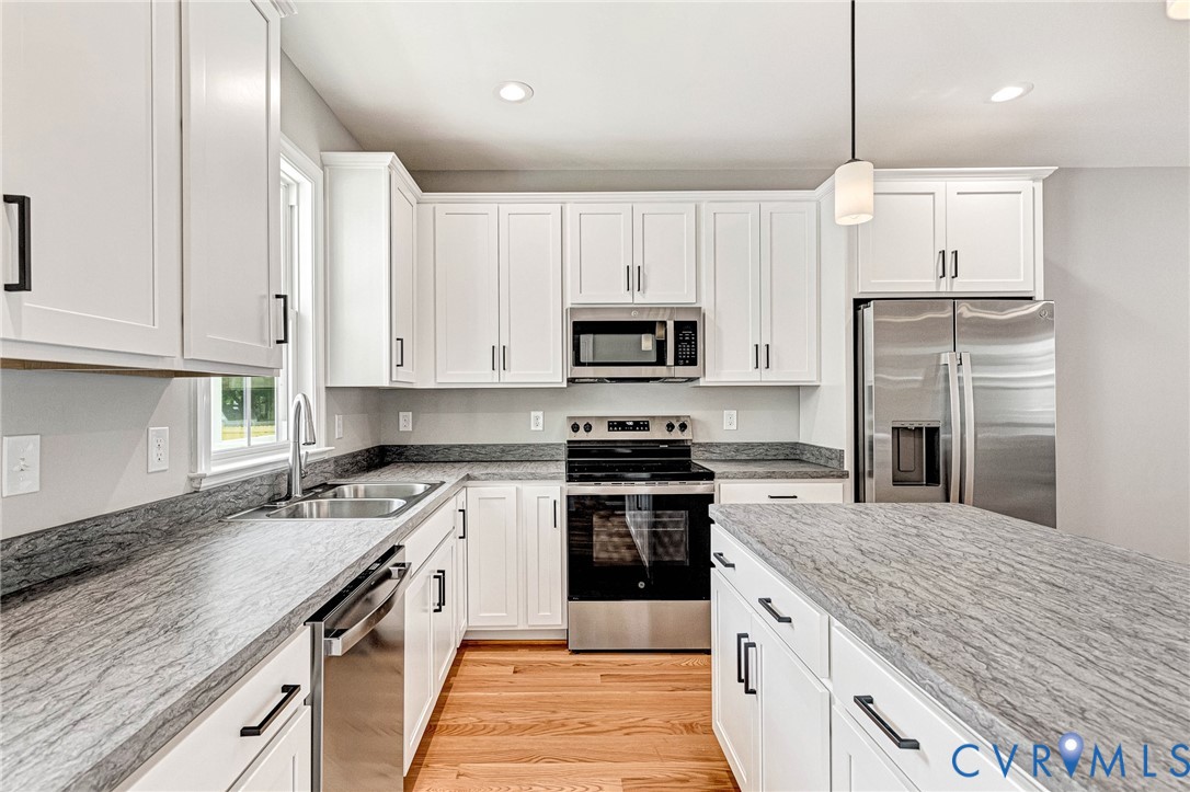 White cabinetry with matte black hardware, stainless steel appliances, light gray patterned countertops, dual basin sink, and wood-finish flooring