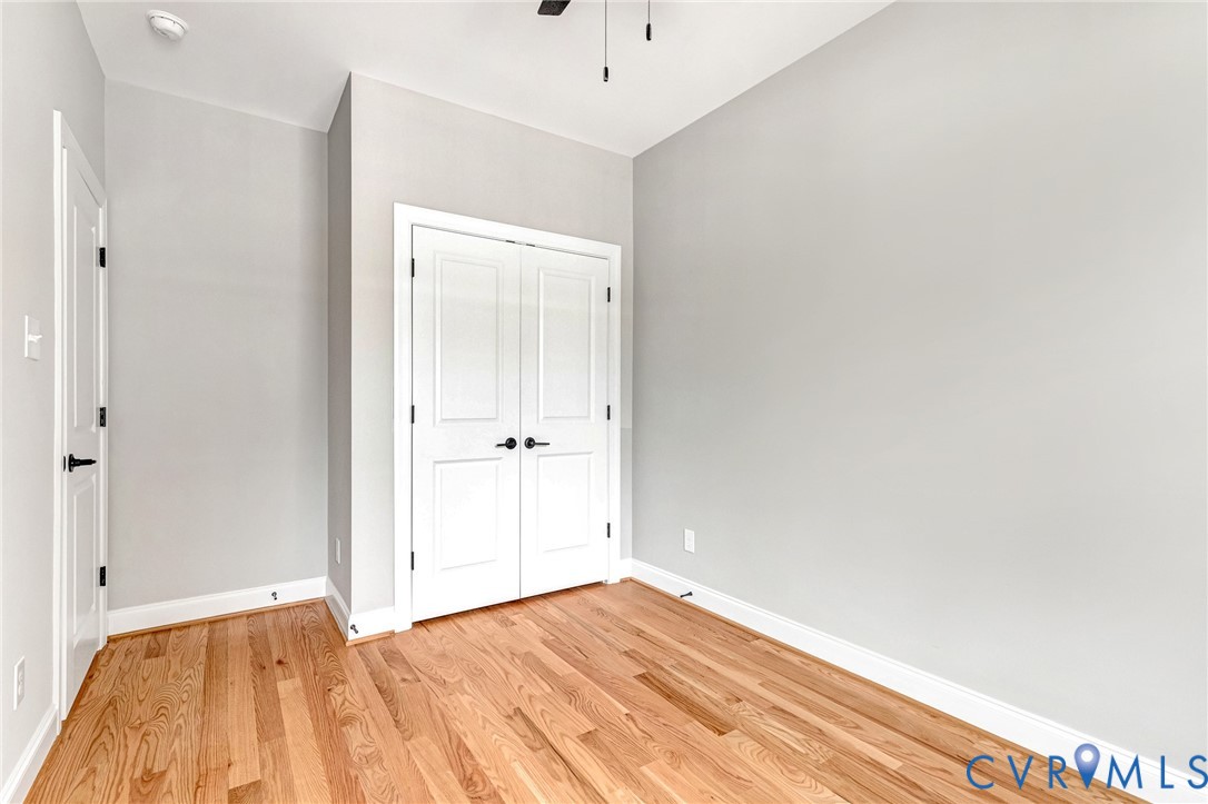 Bright bedroom showcasing gleaming wood-finish flooring, crisp white walls, and ample natural light from multiple windows