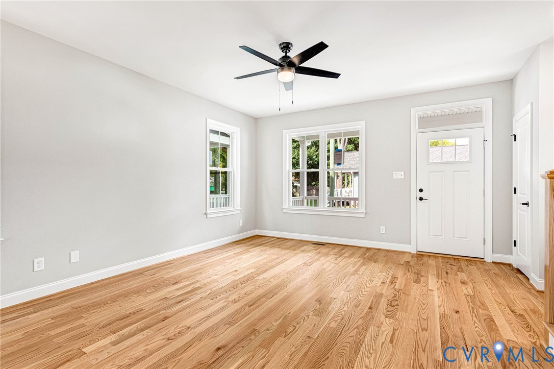 Hardwood flooring, painted walls, ceiling fan with light fixture, multiple windows, and a white entry door with transom window Hardwood flooring, painted walls, ceiling fan with light fixture, multiple windows, and a white entry door with transom window