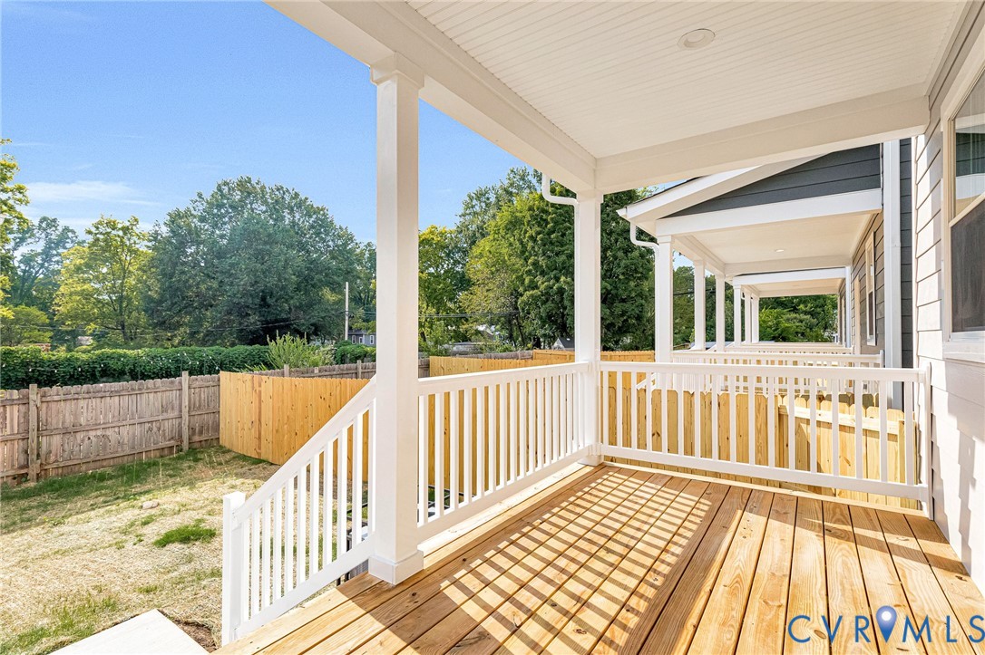 Expansive wood deck with white railings and columns, featuring a white beadboard ceiling with recessed lighting