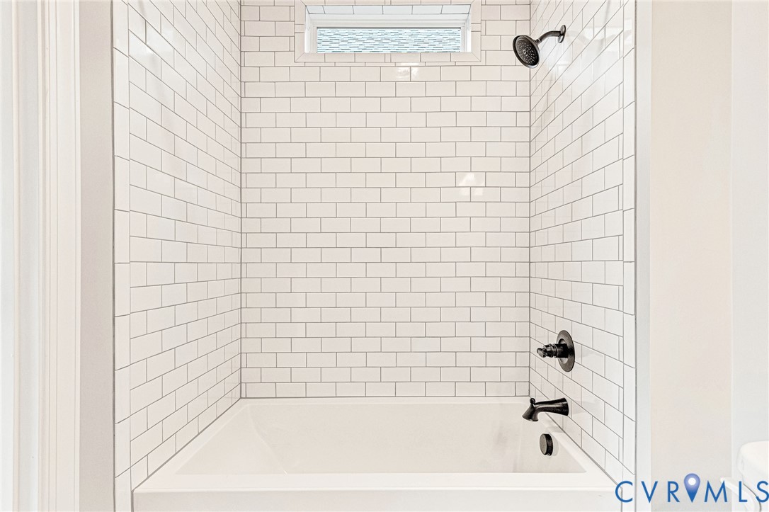 Subway tile shower surround with a built-in tub, transom window, and matte black fixtures