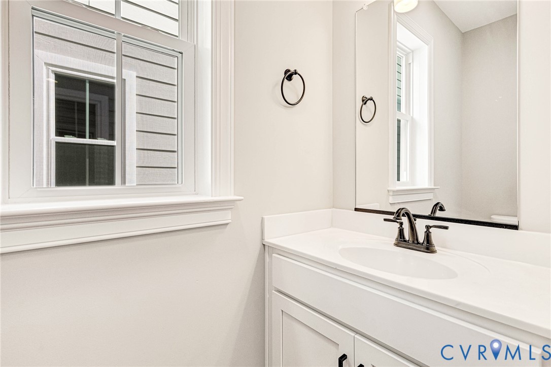 White vanity with an integrated sink and a dark bronze faucet, complemented by a large wall-mounted mirror and a window with white trim