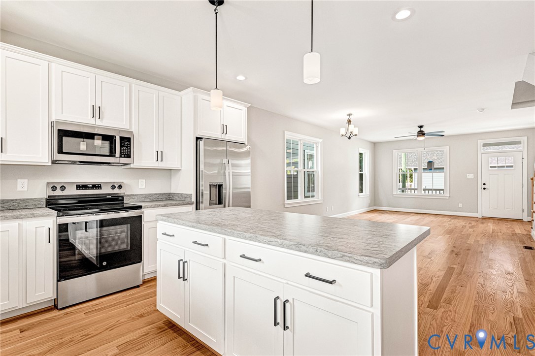 Modern kitchen featuring white cabinetry, stainless steel appliances, a center island with a light-toned countertop, and wood-finish flooring