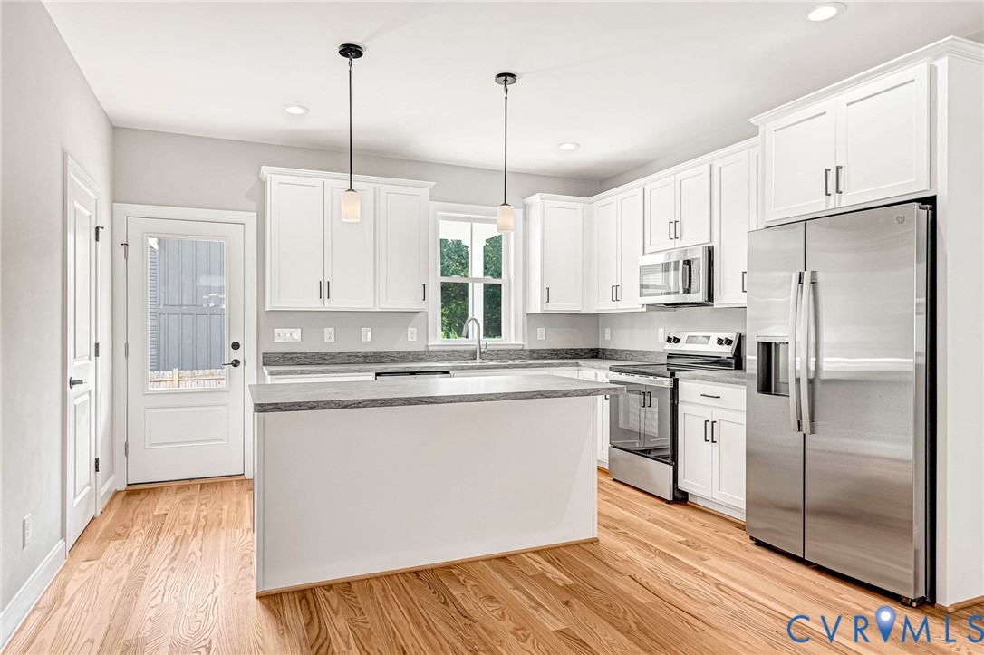 Hardwood flooring, white cabinetry, stainless steel appliances, kitchen island, and recessed lighting