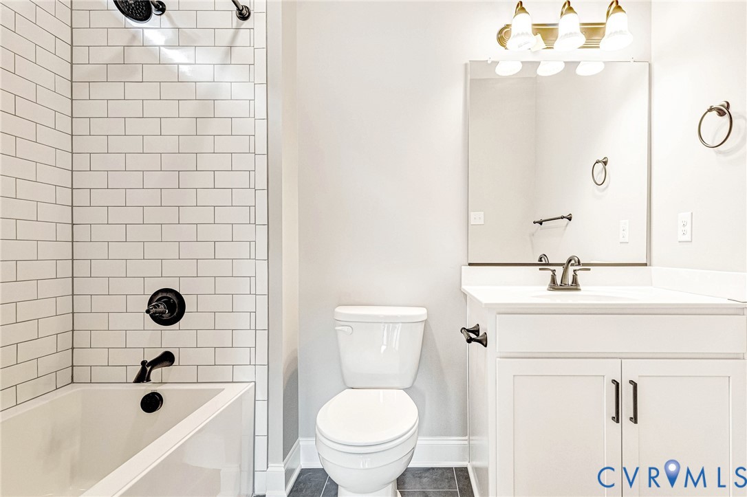 Bathtub with subway tile surround and matte black fixtures, white vanity with integrated sink, rectangular mirror, and dark tile flooring