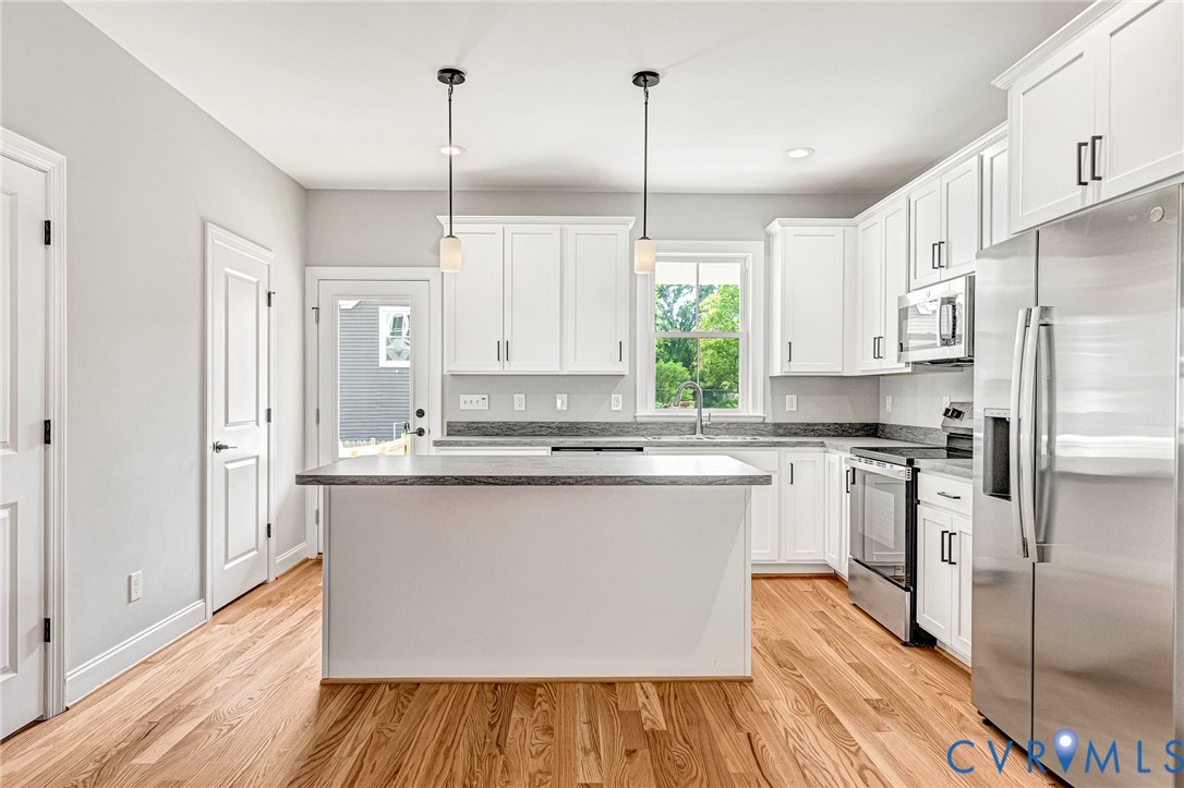 White cabinetry, stainless steel appliances, wood-finish flooring, island with countertop, and pendant lighting
