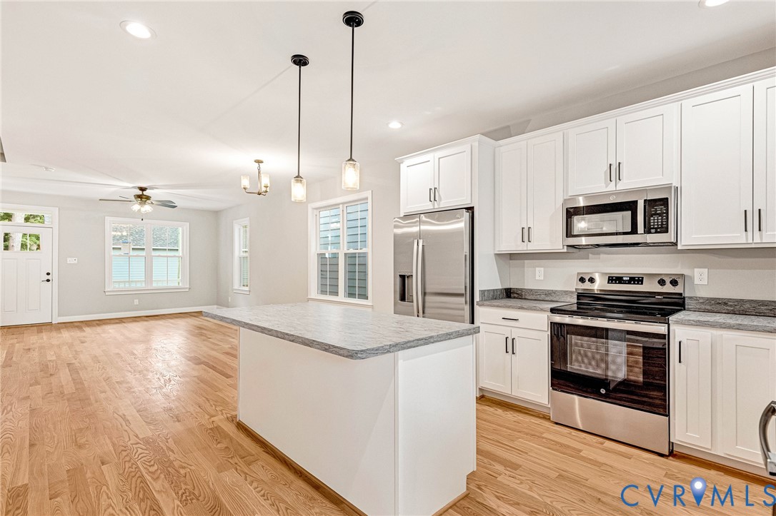 Wood-finish flooring throughout, white shaker-style cabinetry, stainless steel appliances, granite countertops, and a kitchen island with pendant lighting