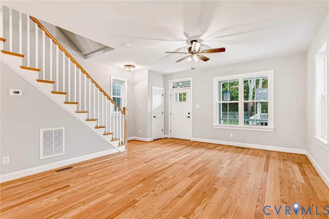 Hardwood flooring, painted white staircase with wood-finish handrail, white trim, ceiling fan with light fixture, and multiple windows