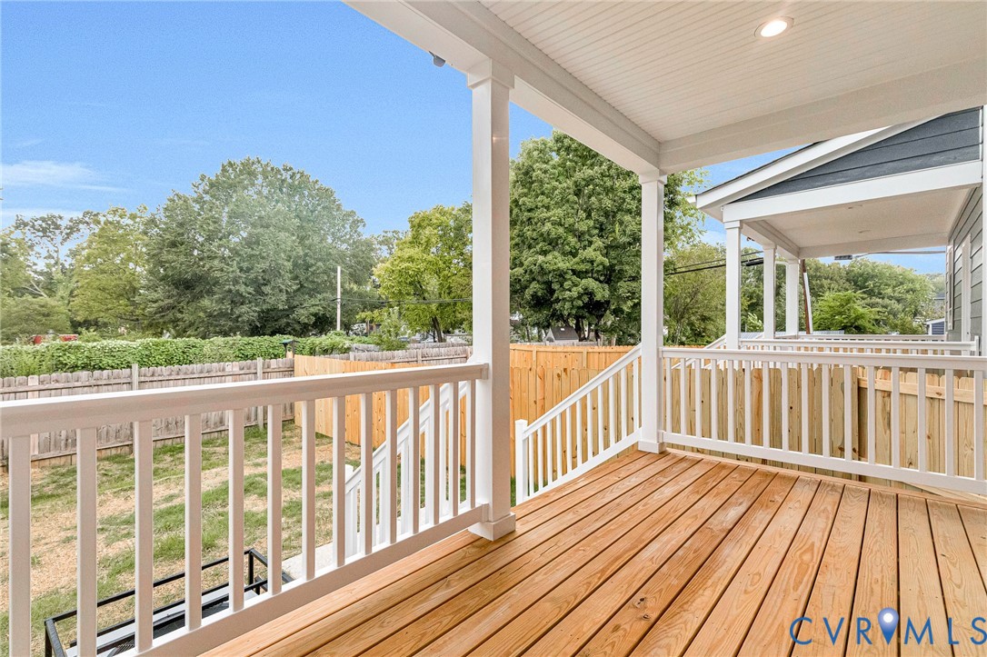 Expansive rear deck featuring natural wood decking, white railings, and recessed lighting in the covered ceiling