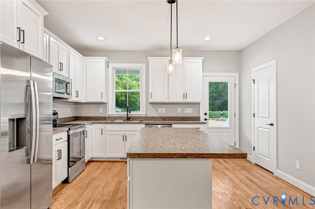 White cabinetry with matte black hardware, stainless steel appliances, wood-finish flooring, and a center island with pendant lighting