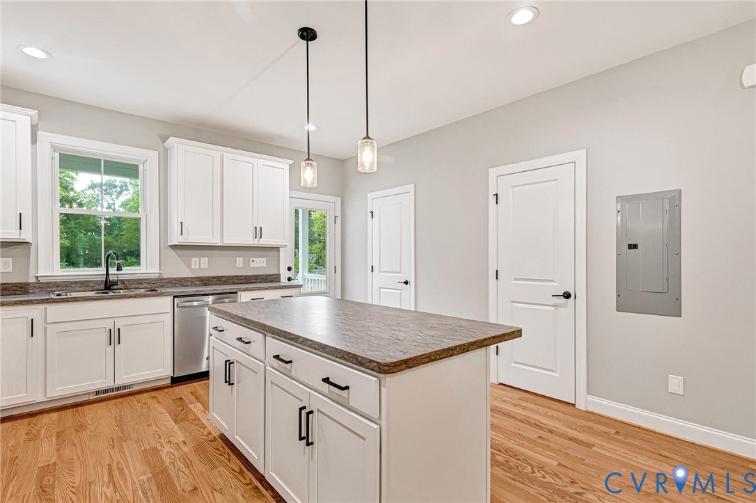 Kitchen with white cabinetry, a center island, pendant lighting, stainless steel dishwasher, and wood-finish flooring